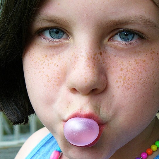 A small girl blowing chewing gum