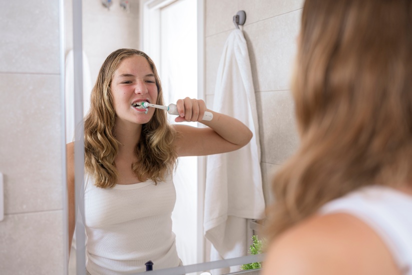 A woman brushing teeth with an electric toothbrush, addressing gum health concerns in Germantown, TN