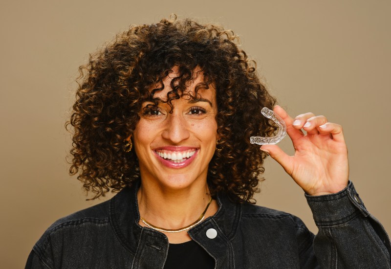 A woman holding a clear aligner, using Candid Clear Aligners for teeth alignment in Germantown, TN