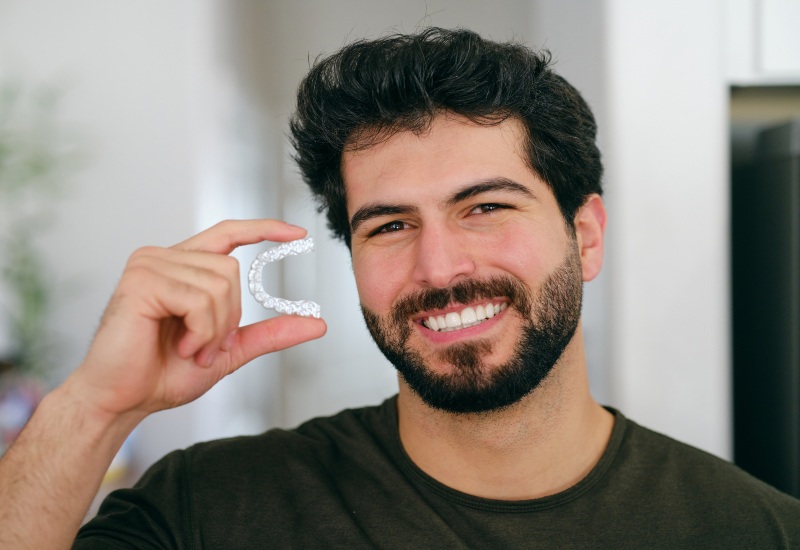 A smiling man holding clear aligners, showing the benefits of Invisalign Aligners in Germantown, TN