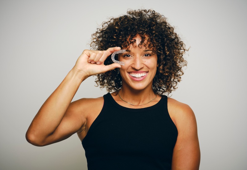 A smiling woman holding clear aligners, starting a confident smile journey in Germantown, TN